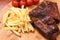 Closeup shot of meat slices, french fries, and tomatoes on a kitchen board