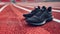 A closeup shot of a pair of sleek black athletics shoes resting on a deep red rubberized track ready to take on the
