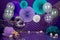 Closeup shot of paper flower decorations, balloons, net, and number 2 on a purple cloth background