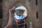 Closeup shot of a person holding a crystal ball with the reflection of historic buildings