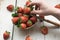 Closeup shot of a person picking a fresh strawberry from a straw bowl on a wooden surface