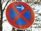 Closeup shot of a red and blue street sign banning parking on a blurred background