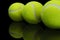 Closeup shot of the reflection of three tennis ball on a reflective black surface