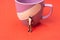 Closeup shot of a small plastic toy person standing in front of a purple cup on a red surface