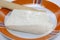 Closeup shot of soft cheese of bovine stracchino on a plate on a white isolated background