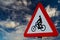 Closeup shot of a triangular red and white sign warns of bicycles against a cloudy sky