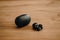 Closeup shot of two modern, wireless, black earbuds and a black earbud case on a wooden surface