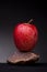 Closeup shot of a vibrant bright red apple on a small piece of rock against a black background