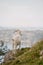 Closeup shot of a white goat from behind at the edge of a high cliff