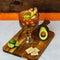 Closeup of a shrimp cocktail on a wooden board next to avocado, crackers, and limes