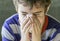 Closeup of sick boy in pyjamas sneezing into a tissue, health co