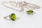 Closeup silver ring and pendant with peridot on white acrylic desk.