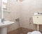 Closeup of simple style interior of small restroom with beige ceramic tile walls, white sink and classic WC toilet
