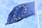 Closeup of single european flag with twelve yellow stars waving in the wind in front of blue sky