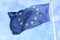 Closeup of single european flag with twelve yellow stars waving in the wind in front of blue sky