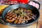 Closeup of a sizzling grilled steak cooked in a black frying pan, served with slices of crusty bread