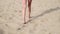 closeup on skinny woman's legs walking with bare feet on sandy beach, sunbathing