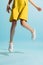 Closeup slender female legs in summer dress and white sneakers hover above the floor isolated on blue background