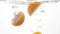 Closeup slow motion footage of tropic citrus fruits halves falling and splashing in cold clear water