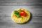 Closeup of a small load of bread spread with hummus, with a slice of tomato on a gray blurred background.