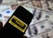 Closeup of smartphone screen with logo lettering of online money transfer service western union, blurred banknotes background