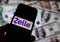 Closeup of smartphone screen with logo lettering of online money transfer service Zelle, blurred banknotes background