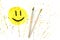 Closeup smiley symbol with paint brushes on yellow spray background