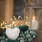 Closeup of snowball in shape of heart in hands with mittens and outdoor candle holder with burning candle