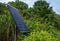 Closeup of solar panel operating in a green nature surrounding trees and ornamental bushes