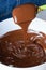 Closeup of a spatula with tempered chocolate falling into a white bowl