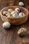 Closeup of speckled quail eggs in unfocused wooden bowl and loose eggs on wooden table in portrait