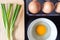 Closeup spring onion on wood butcher and fresh chicken egg in bowl and group of egg in box on wooden kitchen table for healthy and