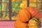 Closeup of a stack decorative colorful pumpkins on a table with a red tablecloth over open windows with an abstract blurred