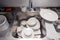 Closeup stack of dirty dishes at bottom of metal square sink at professional restaurant kitchen: white ceramic stack of plates,