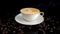 Closeup of a steaming hot cup of coffee on a black surface. Cup of cappuccino and coffee beans on a black surface
