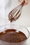 Closeup stirs milk melted chocolate in glass bowl with whisk, white background