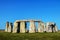 Closeup of Stonehenge standing stones with three lintels across four huge uprights in the foreground under a very blue sky on a