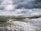 Closeup of a stormy sea making foam on the beach, gloomy, cloudy sky background