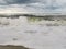 Closeup of a stormy sea making foam on the beach, gloomy, cloudy sky background