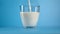 Closeup stream organic milk pouring transparent glassware isolated on blue studio background slowmo