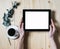 Closeup tablet with a empty blank screen monitor in the girls hands with a branch of eucalyptus and a cup of coffee on table