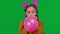 Closeup teen girl blowing pink balloon looking at camera at green screen. Cheerful Caucasian teenager celebrating