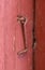 Closeup of textured red door with a rusty metal hook. Bright wooden doorway and doorframe aged with cracked patterns