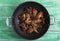 Closeup of a thai recipe with caramelized chicken wings in a wok pan on green wooden table