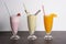 Closeup of three vibrant smoothie glasses lined up side-by-side on a plain surface