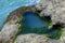 Closeup of a tidepool filled with water in the rocks by the ocean, rimmed with green algae.  The algae appears as a miniature