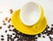 Closeup tilt ankle yellow ceramic coffe cup on yellow plate,plenty of coffee beans around