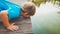 Closeup toned portrait of adorable toddler boy kneeling at river and looking at water strider floating on lake surface