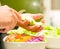 Closeup tuna salad with fresh purple cole, tomato and capsicum slices in white bowl, hand holding avocado pieces above