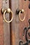 Closeup of two antique copper ornate door knockers over an aged wooden door.